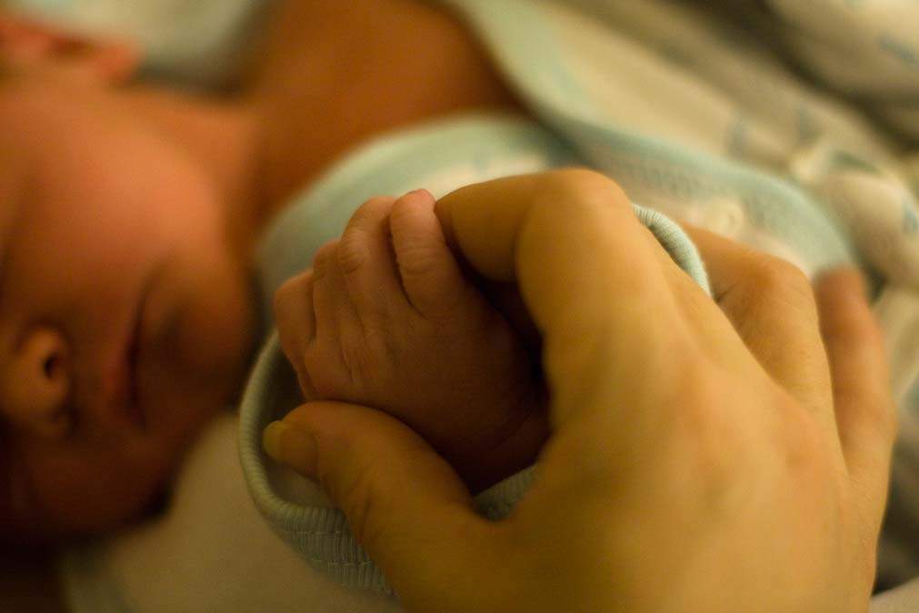 parent holds infant's hand