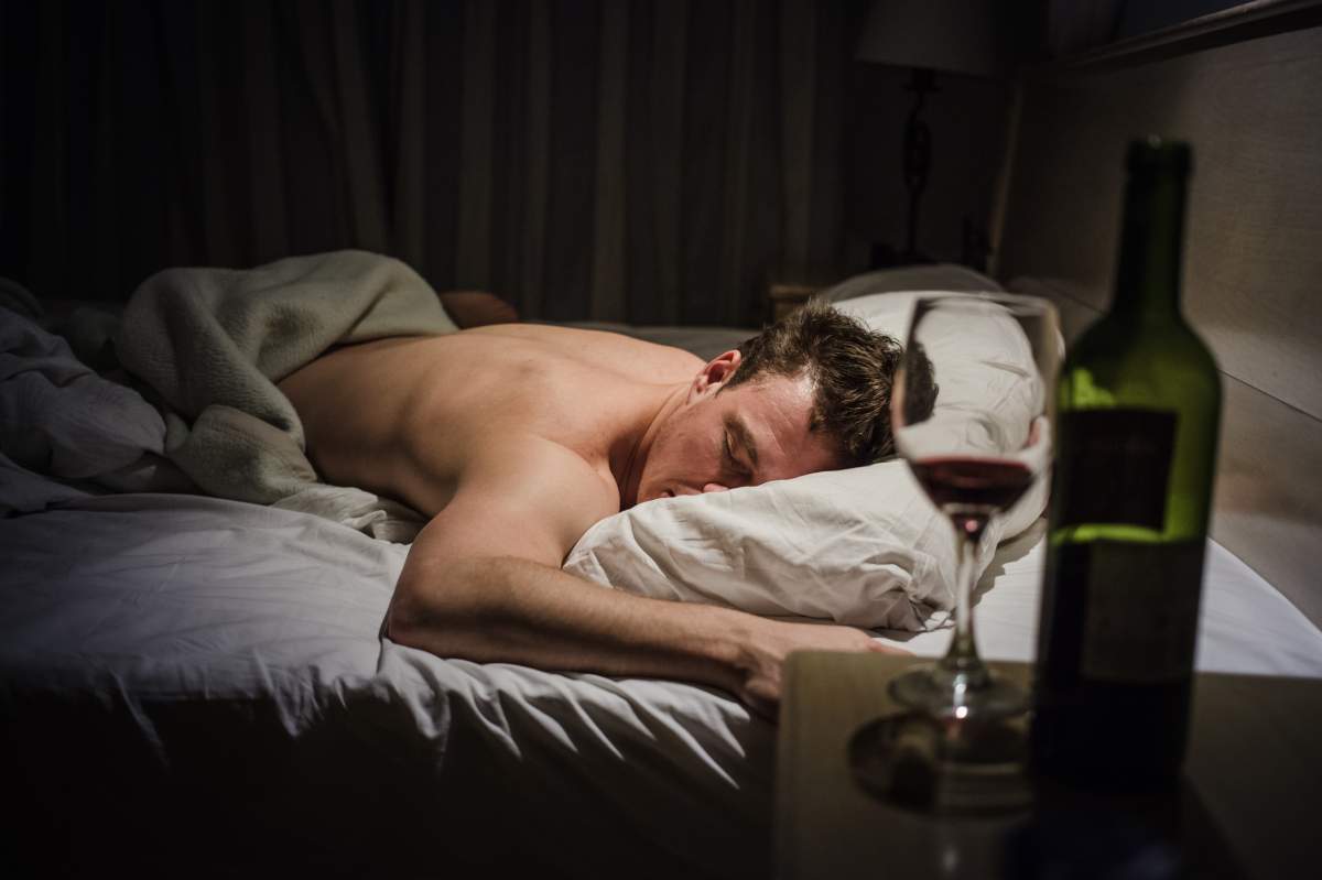 man in bed next to empty glass of wine and wine bottle