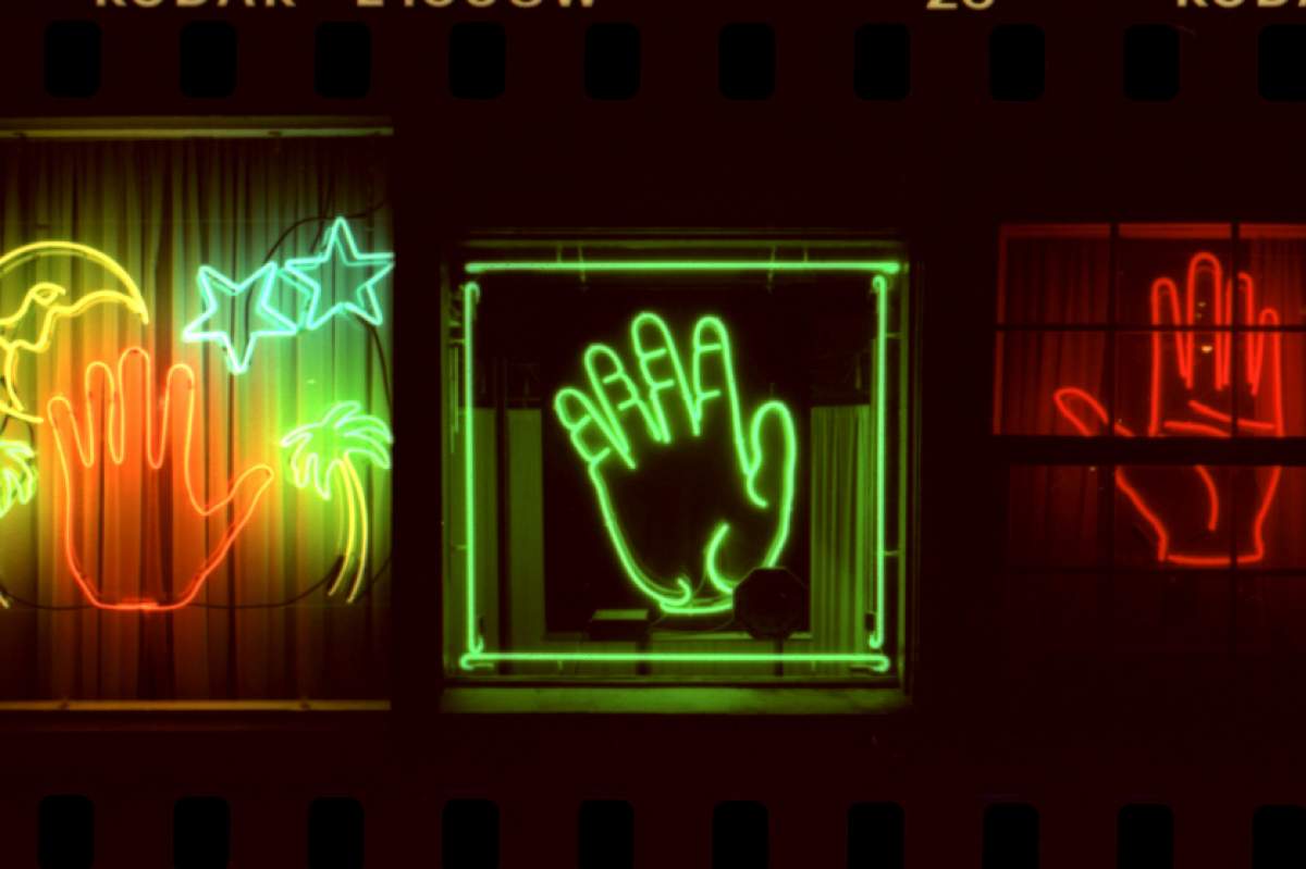Three neon lights in the shapes of hand. The left is orange-red. The middle is bright green. The right is red.