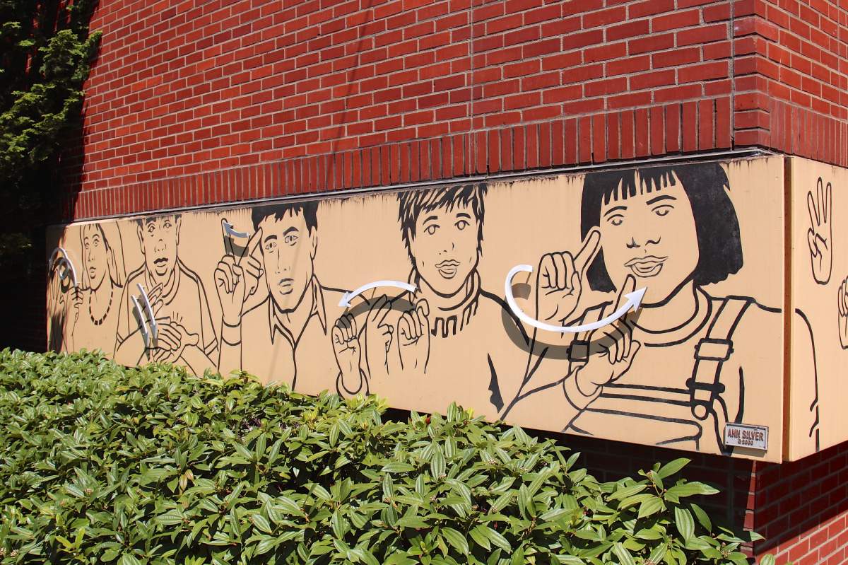 The side of The Washington School For The Deaf. The top of the building is red brick. The photo's main feature are illustrations of people using American Sign Language.