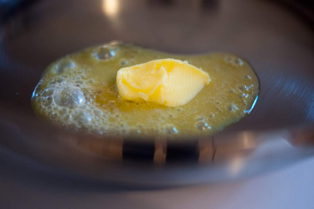 A close-up of a tablespoon of butter melting in a pan.