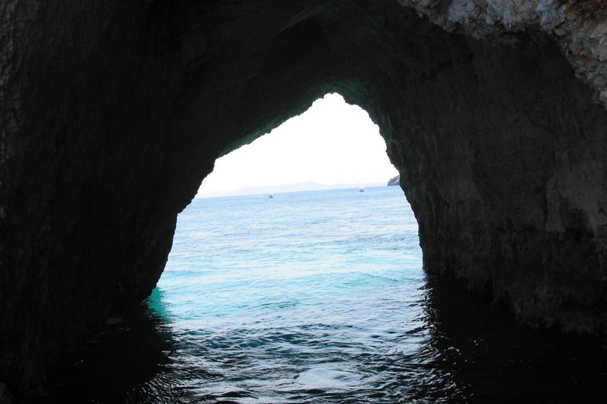 Image taken from inside a cave outside of Zakynthos. The dark cave wall with an opening. The water is dark blue within the cave, lighter and lighter blue in the distance.