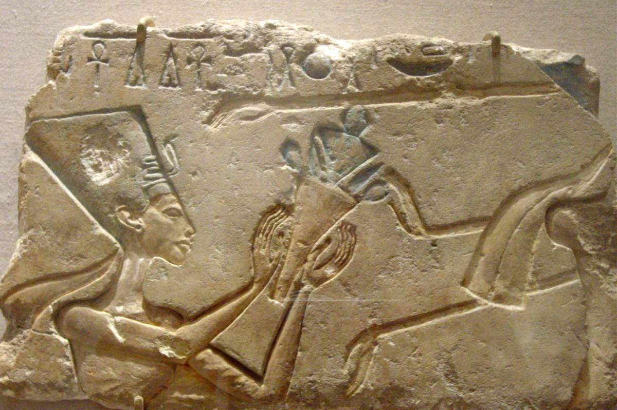 A Stone etching of Nefertiti holding a jug with other hieroglyphics surrounding her.