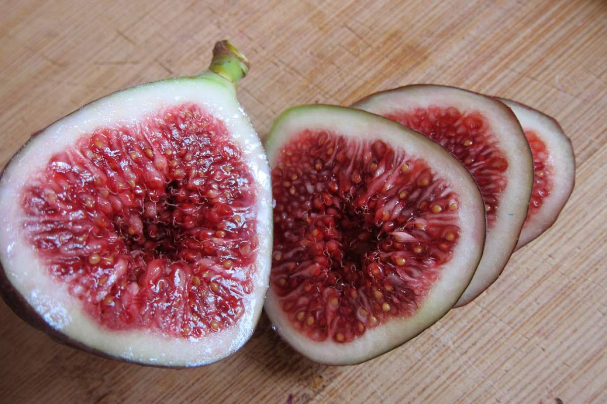 Two figs cut in half. There is a small indentation in each visible fig center. The figs' insides are magenta-pink with a white layer surrounding them.