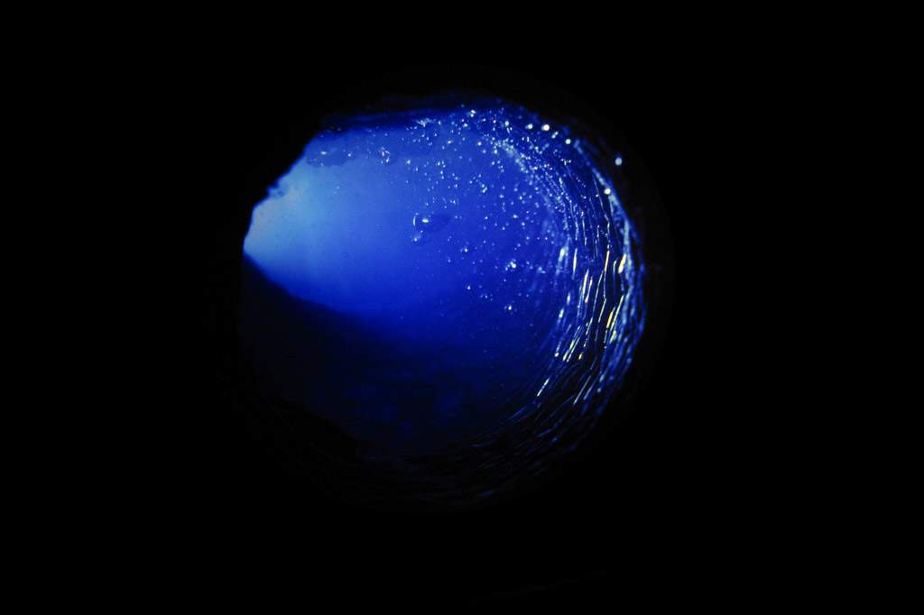 A mostly black image. In the center of the image is a hole that is illuminated by royal blue light.