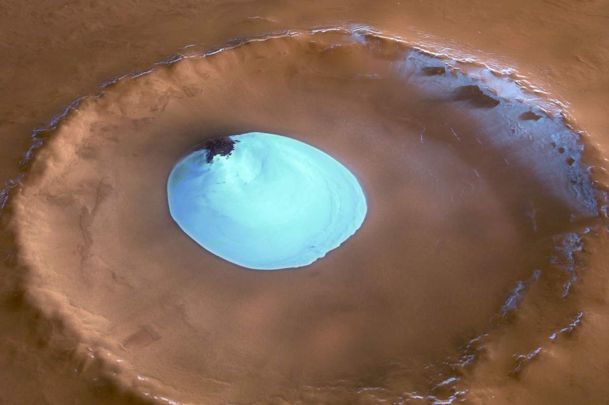 A Martian crater, the ground is rust colored. Near the center of the image is a light (but also bright) blue circle that is the crater water ice.