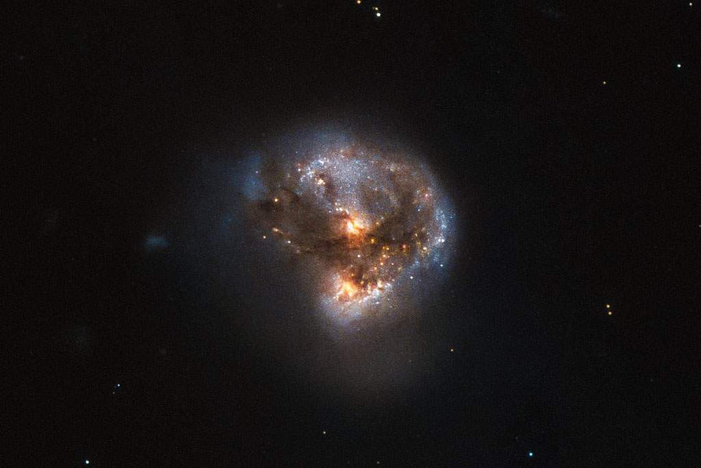 A circular looking galaxy is in the center of the screen. It is orange and blue. The background is deep black.