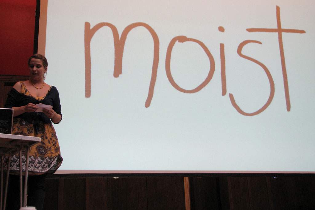 A woman next to a white board with the word moist written on it in big letters.