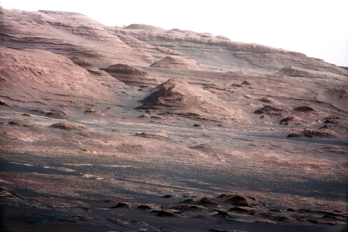 From the source: "In the distance, there are dark dunes and then the layered rock at the base of Mount Sharp. Some haze obscures the view, but the top ridge, depicted in this image, is 10 miles (16.2 kilometers) away."