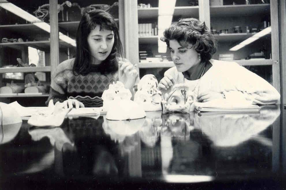 a black-and-white photograph of two women looking at a taken apart model skeleton