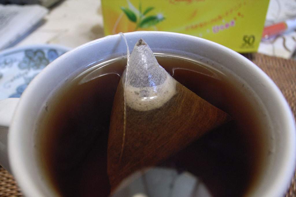 a pyramid tea bag in a cup of dark brown tea