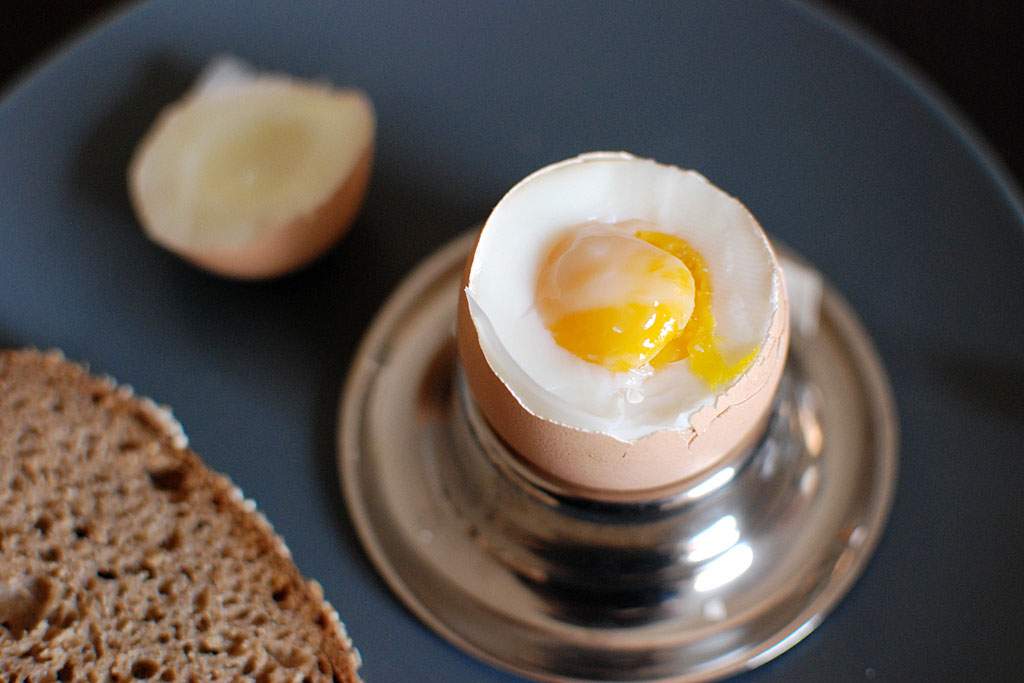 a soft boiled egg in a cup, and a piece of toast on a plate.