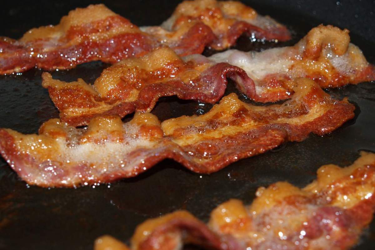four strips of bacon sizzling in a black pan