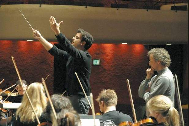 A conductor in profile raises both arms leading an ensemble