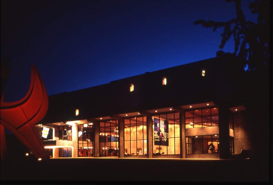 the exterior of a large concert hall at night. a large sculpture stands in front of the building.