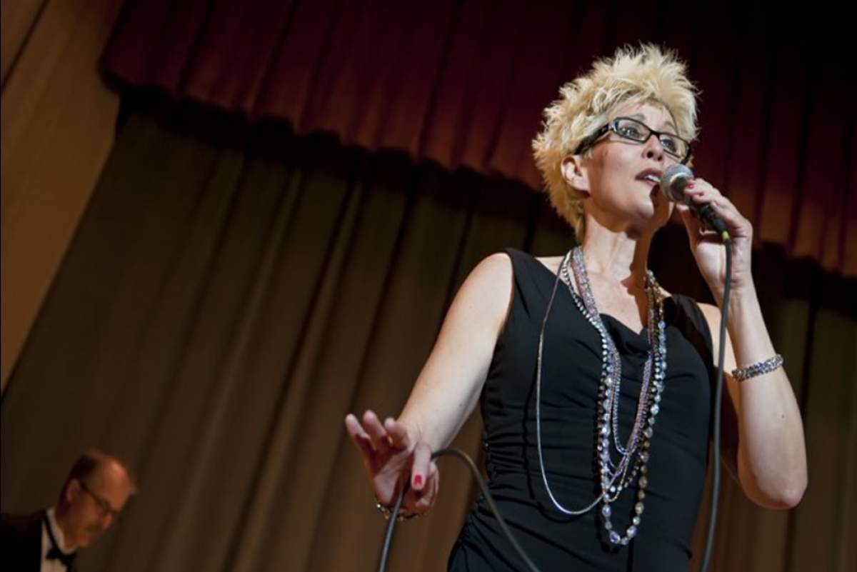 A woman in glasses sings into a microphone