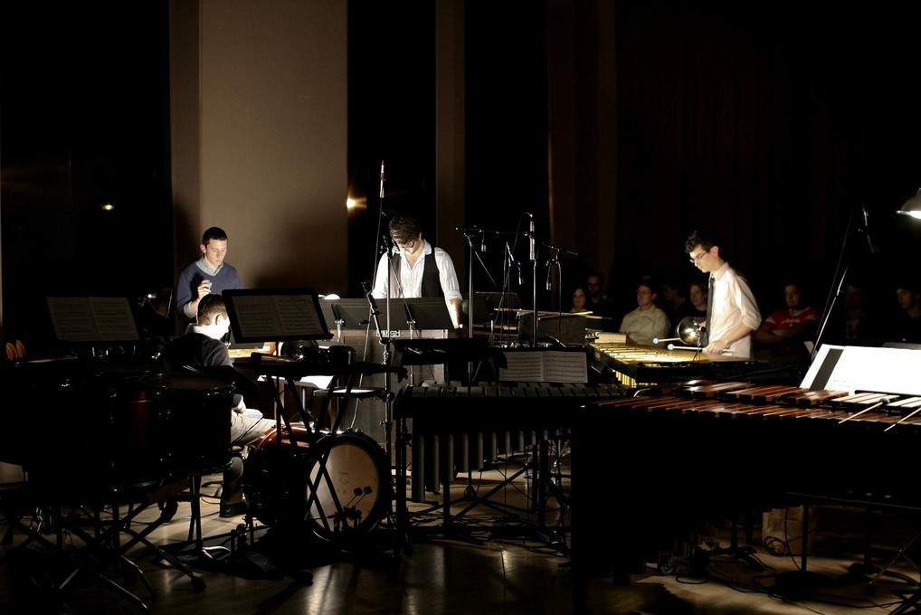 a group of percussionists play various instruments on a darkened stage