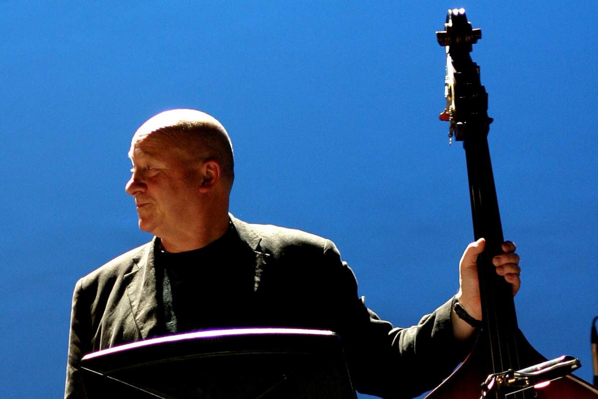 A man holds a double bass in front of a blue backdrop
