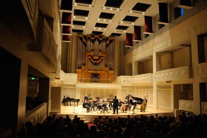 A chamber orchestra performs on stage in a darkened concert hall