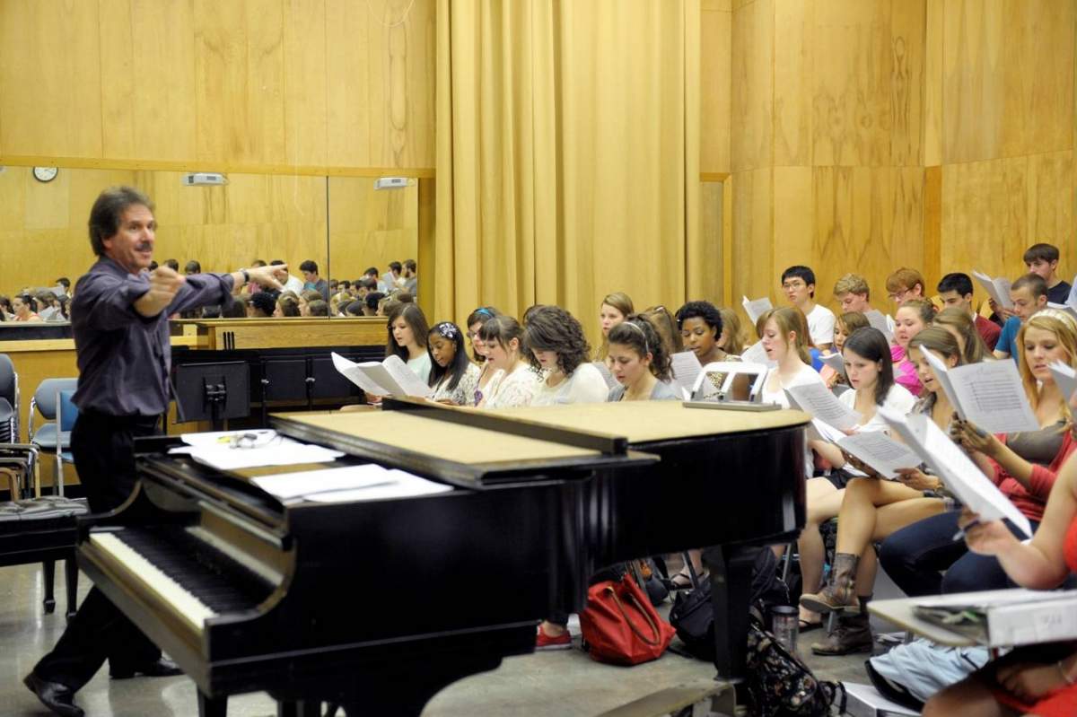 A man directs a seated choir in rehearsal