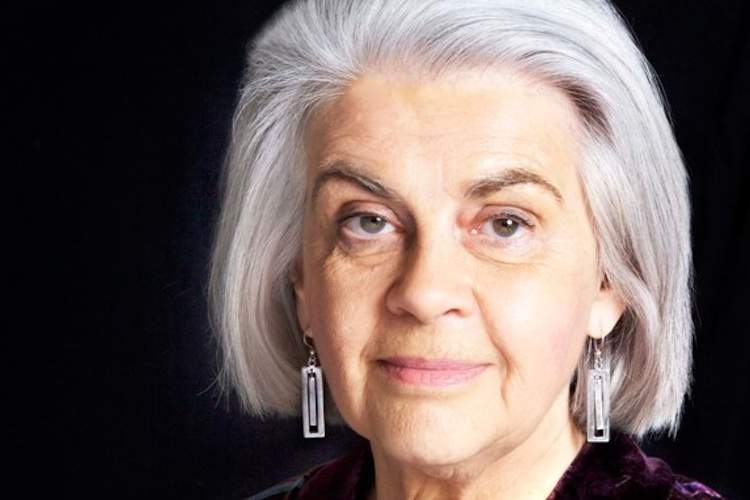 A woman with gray hair and earrings looks into the camera