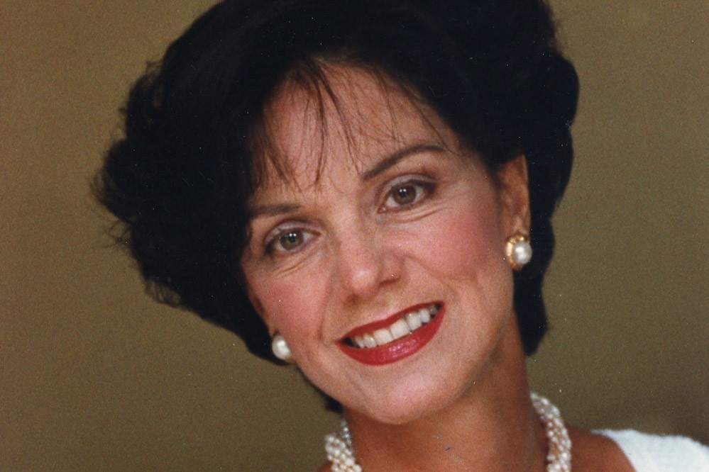 A woman wearing pearl earrings smiles into the camera