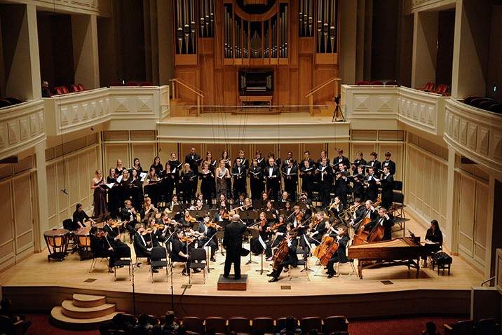 a chorus and orchestra perform on a dimly lit concert stage