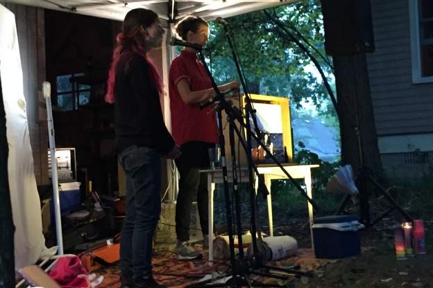 Two women sing and tell stories in front of a small audience in a Bloomington backyard
