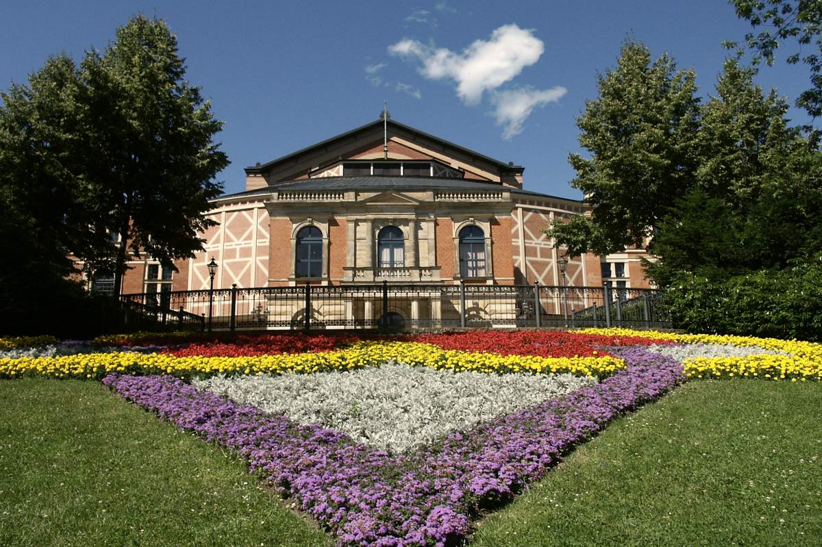 Flowers bloom in a manicured triangle in front of a pink brick opera house