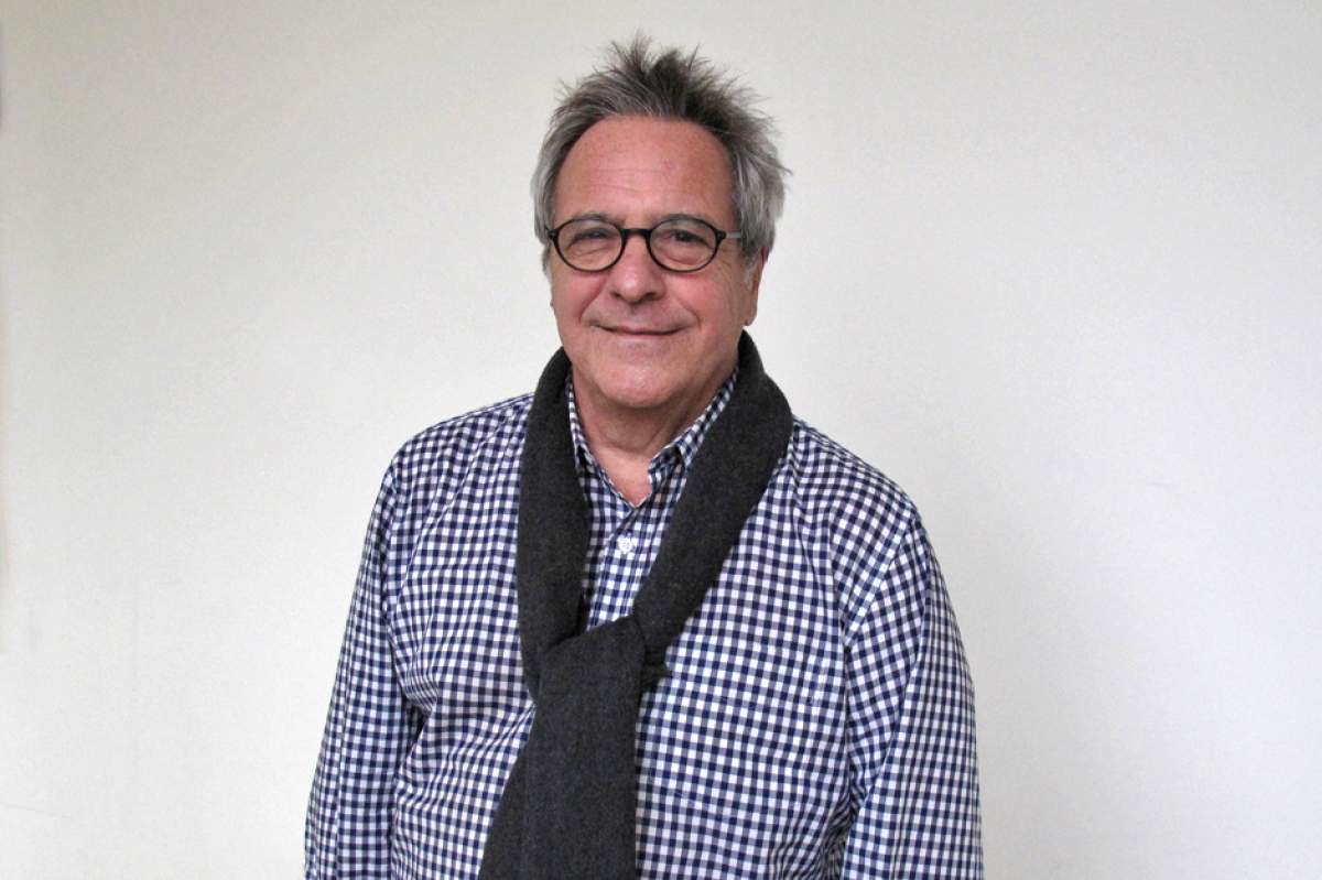 David Anspaugh in glasses, blue-and-white checked shirt, navy blue sweater draped around his shoulders