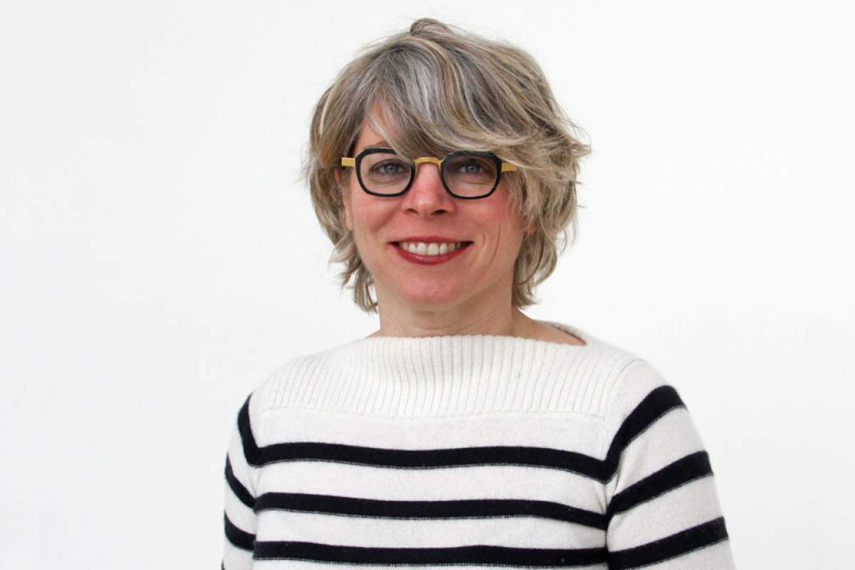 Jill Lepore wearing white sweater with black horizontal stripes, her hair covering forehead and touching black horn-rimmed glasses.