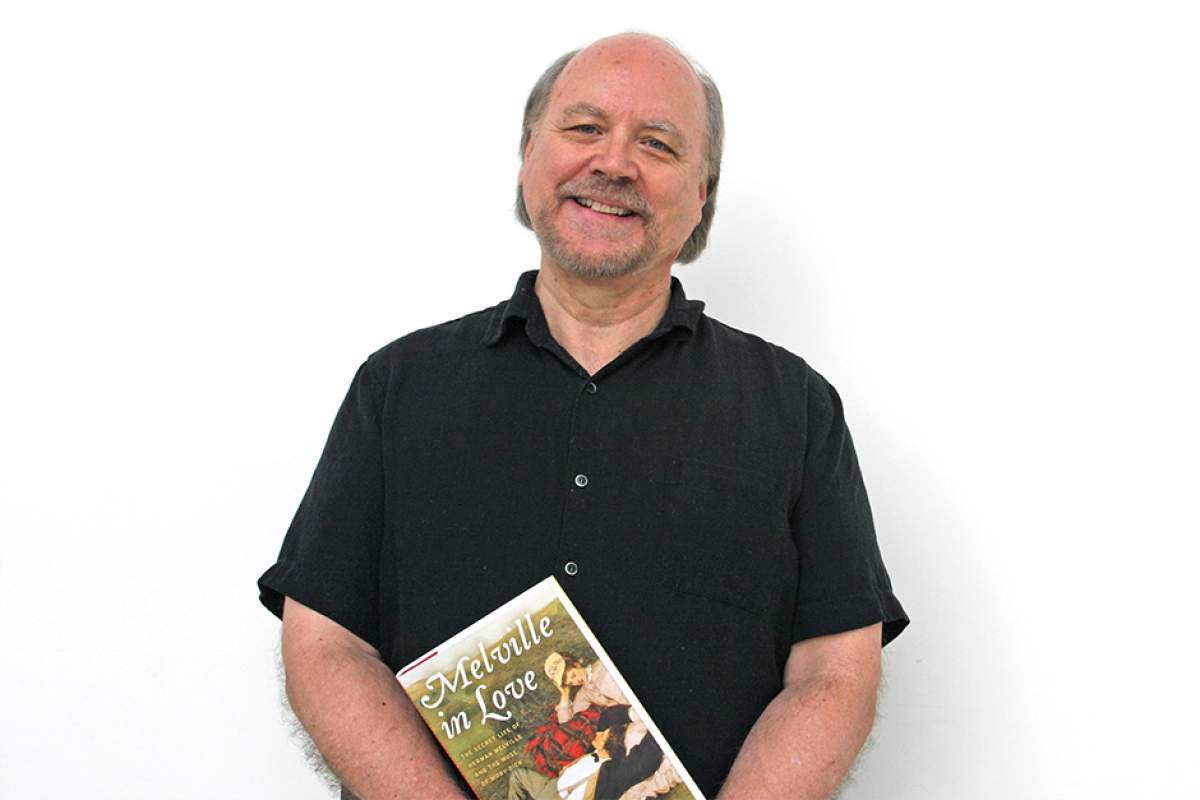 Michael Shelden in black polo shirt, smiling, holding a copy of Melville in Love.
