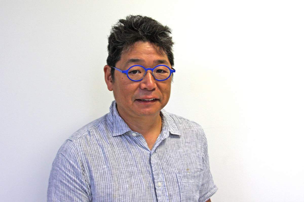 Osamu James Nakagawa in wearing round, blue-framed glasses and short-sleeved shirt.