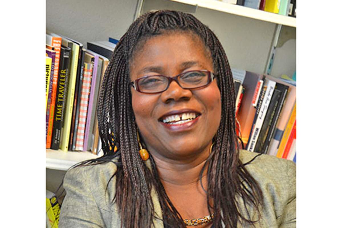 P. J. Wesley, smiling, in glasses with hair in braided cornrows, books in bookshelf behind her.