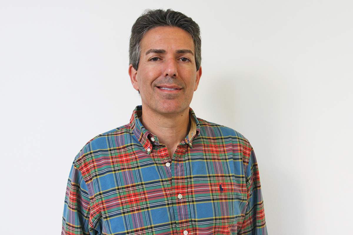 Wayne Pacelle wearing a casual red and blue checked long-sleeved shirt, showing a crooked smile