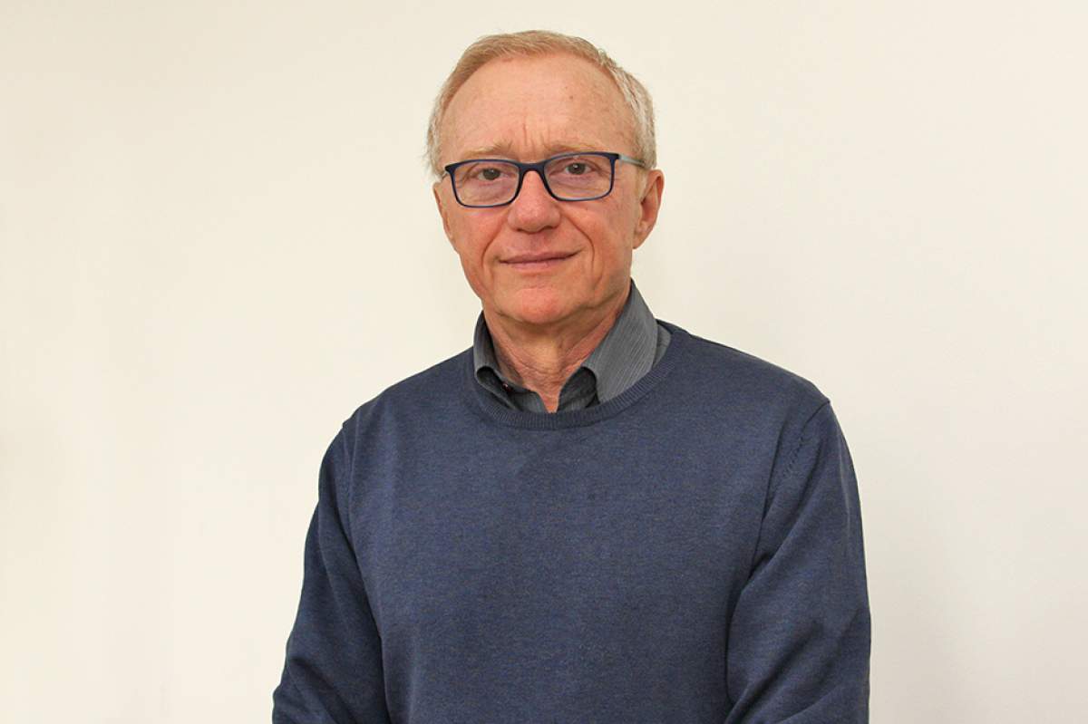 David Grossman, wearing glasses, in a dark blue sweater over a gray striped shirt unbuttoned at the neck.