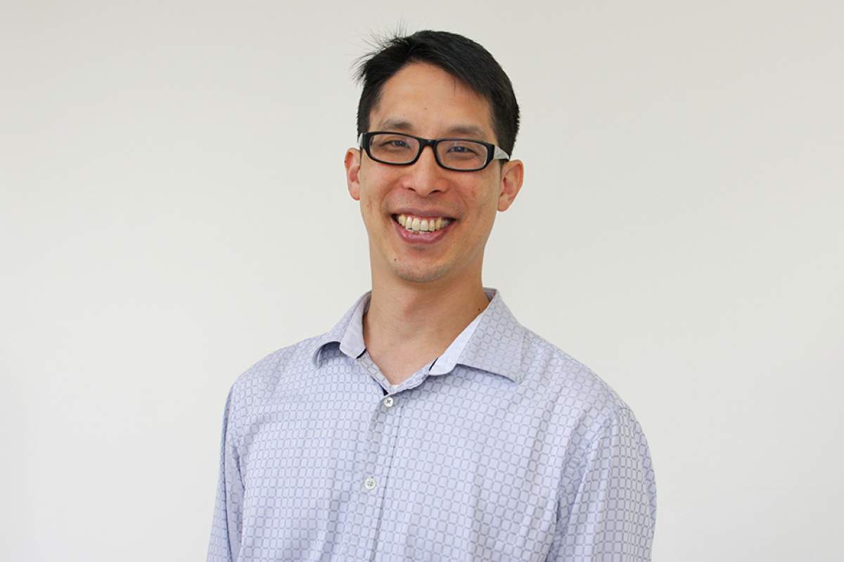Gene Yang, smiling, in black hornrimmed glasses and off-white dress shirt with grey square pattern open at the neck.