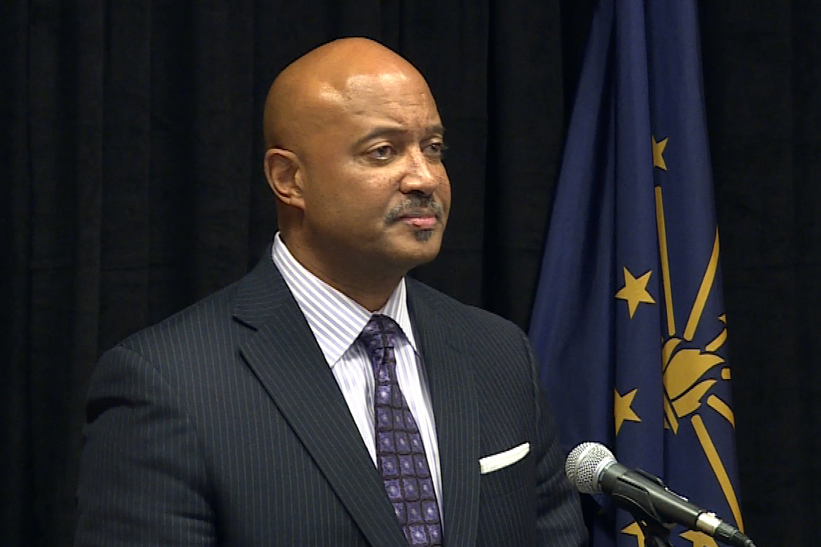 Curtis Hill stands at a podium with the Indiana flag behind him.