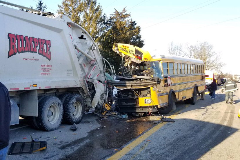 A school bus with a crumpled front end just behind a Rumpke garbage truck