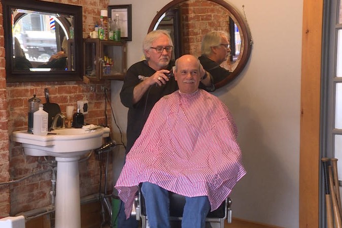 A man cuts another man's hair in a barbershop.