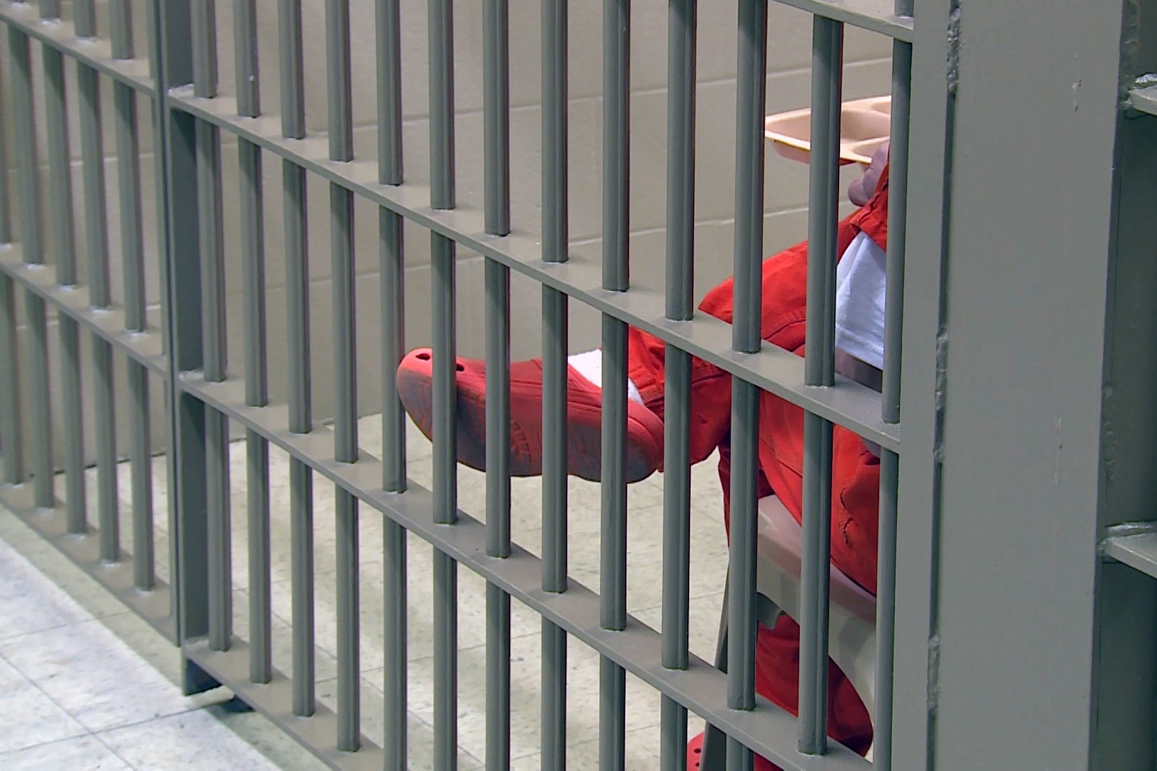 A person in an orange prison outfit sits in cell eating lunch