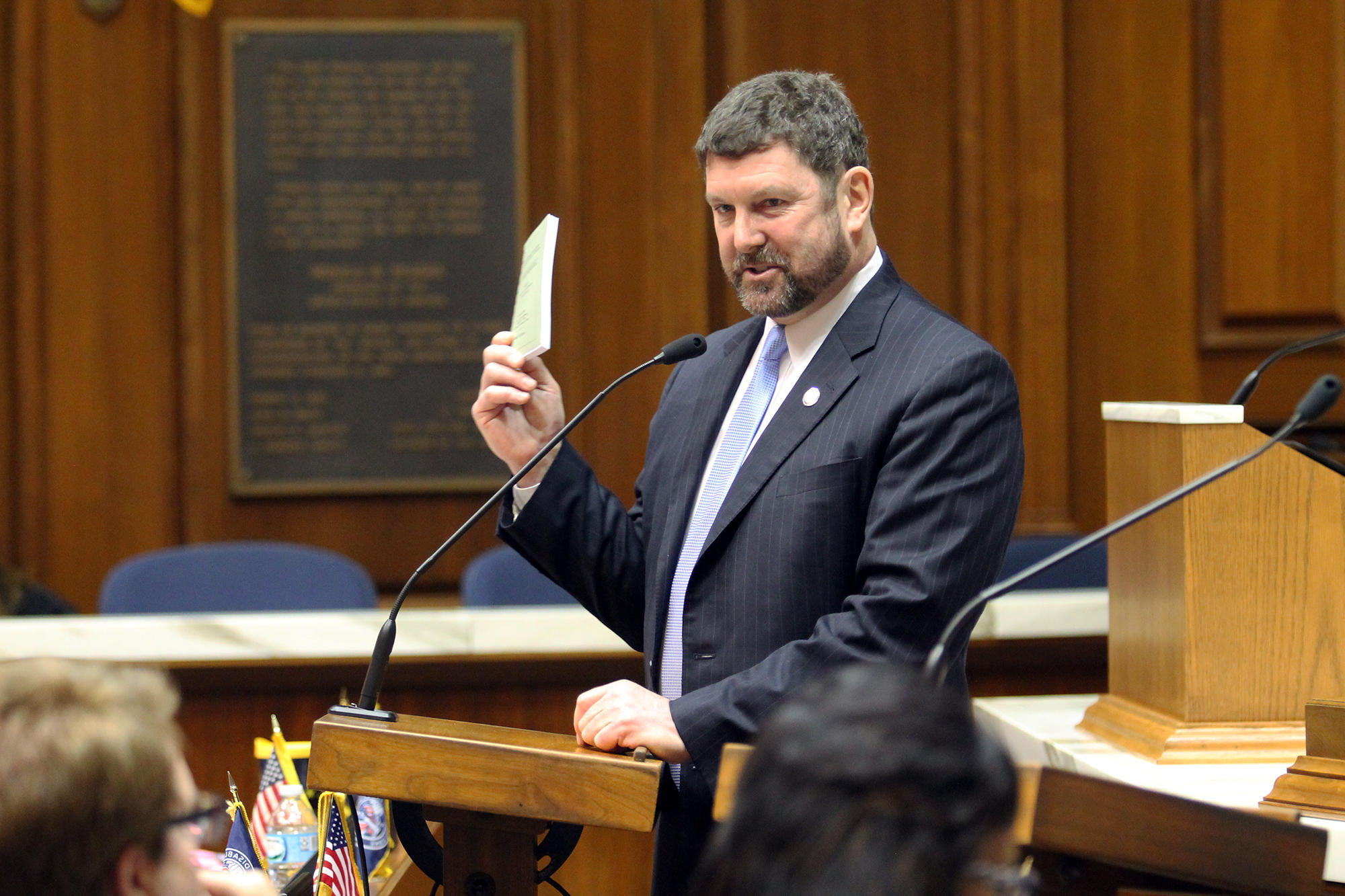 Rep. Jim Lucas speaks at a podium at the Statehouse and holds up a small booklet.
