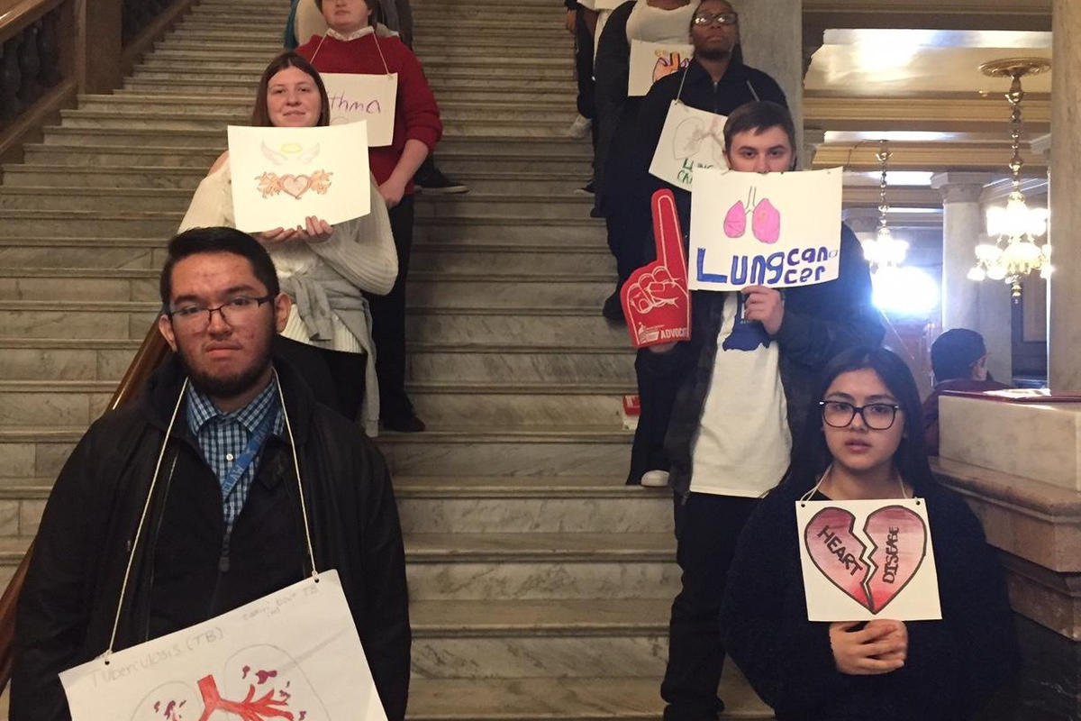 Teens stand on a staircase holding signs about heart disease and lung cancer