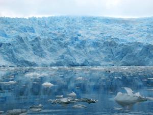 A glacier wall of blue ice rises against a grey sky