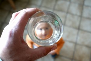 A man holding a glass over a small child so the child's face shows in the bottom of the cup