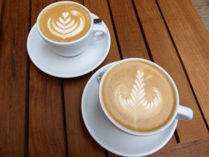 Two lattes on a wooden table with leaf designs on their surface
