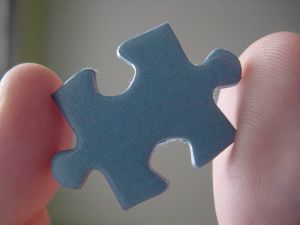 A blue puzzle piece held between two finger tips