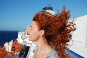 A woman with red hair stands on a boat deck, her hair blowing in the wind