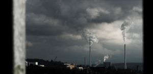 Two large chimneys with large white clouds coming out of them, going into the overcast sky