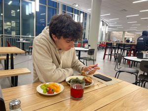 Alexei Liebrum eating a meal at table with wooden top, in a large, well lit dining hall